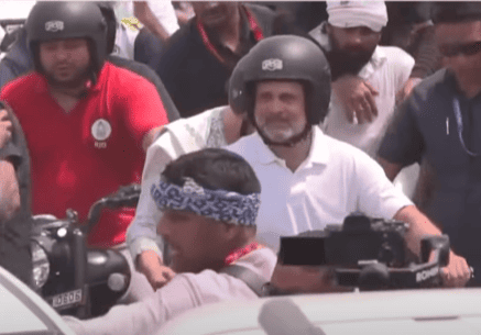 A group of people, some wearing helmets, navigate through a crowd with motorcycles on a busy street during the daytime.