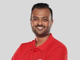 A man in a red polo shirt smiles warmly at the camera.
