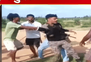 A group of men, including one in a military uniform, are engaged in a confrontation outdoors on a dirt path.