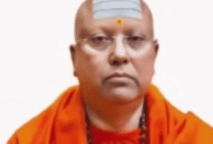 A man with a white dot on his forehead, looking directly at the camera with a neutral expression.
