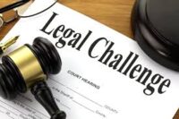 A document titled "Legal Challenge" on a desk, with a judge's gavel and glasses placed nearby.