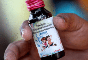 A hand holds a small bottle of cough syrup with a pink cap. The label features cartoon children and medicine details, conveying a sense of care and healing.