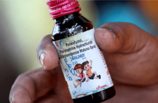 A hand holds a small bottle of cough syrup with a pink cap. The label features cartoon children and medicine details, conveying a sense of care and healing.