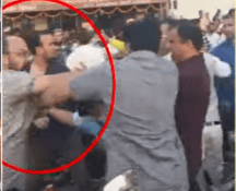 A crowd of people engaged in a physical altercation, with two men in the foreground pushing each other. The scene is chaotic and tense.