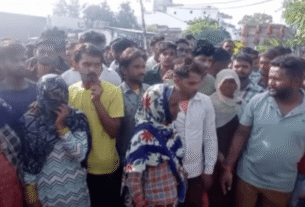 A large group of people gathered outdoors, some looking towards the camera. They appear engaged and curious, with varied expressions and clothing.