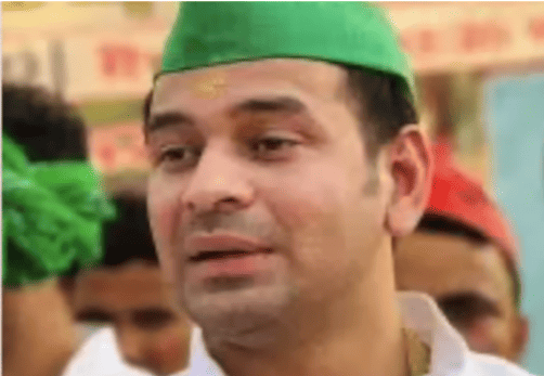 A man wearing a green cap, white shirt, and gold mark on forehead, stands among a crowd. The mood appears calm and attentive.